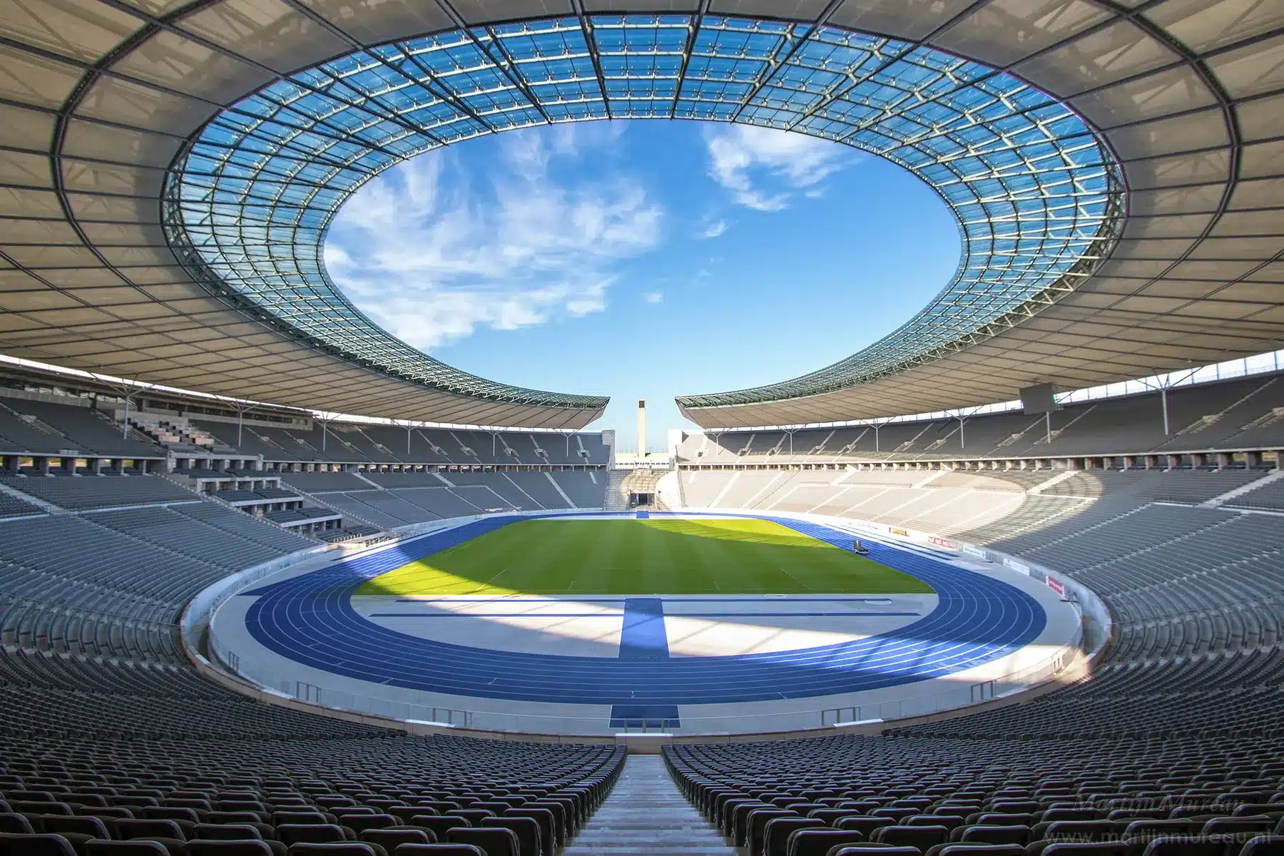Weitwinkelansicht des leeren Olympiastadions in Berlin mit blauer Laufbahn und dem charakteristischen Stadiondach.