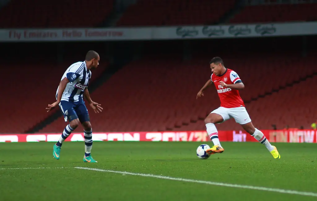Serge Gnabry in einem roten Arsenal-Trikot beim Dribbeln mit dem Fußball auf einem Spielfeld.